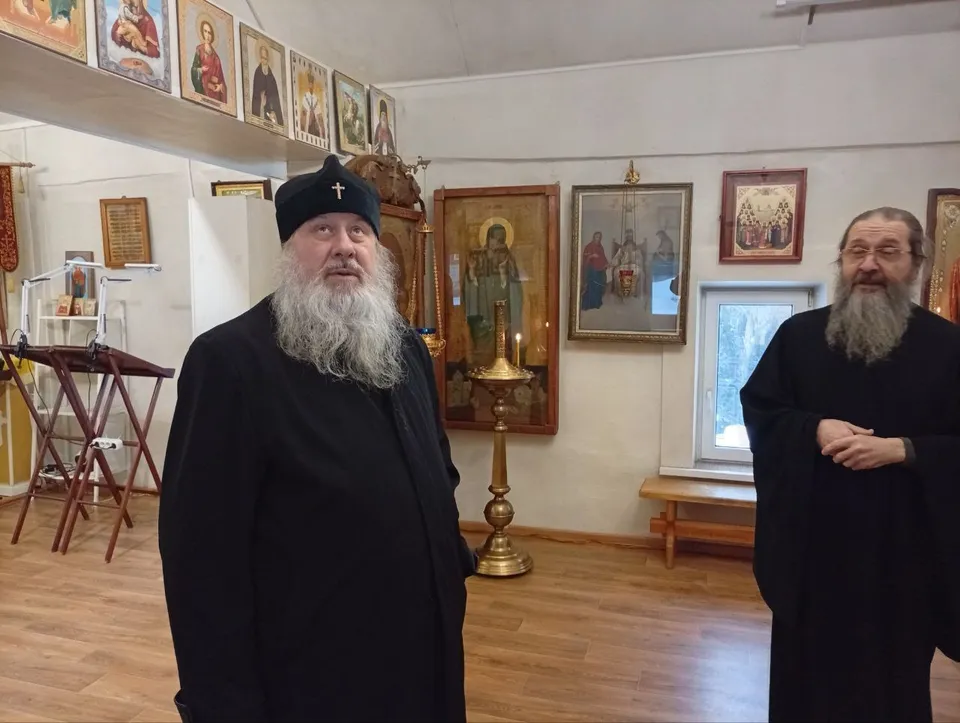Двое священнослужителей в чёрном в помещении храма, на стенах иконы