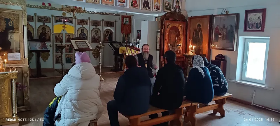 Священник беседует с несколькими молодыми людьми, сидящими на скамье в храме