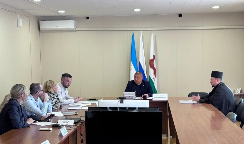 Совещание в кабинете администрации: чиновники и священник за столом обсуждают выделение участка