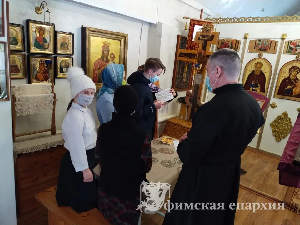 Священник и дети в масках рассматривают старинные иконы у аналоя в храме